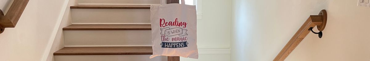 Bookish canvas tote bag with a printed quote, "Reading is when the magic happens," hanging from a stairway banister at a cozy retreat home